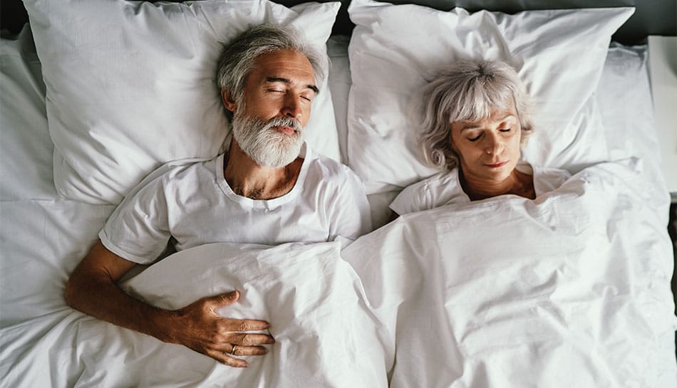 mature couple sleeping in bed peacefully together as light shines through window