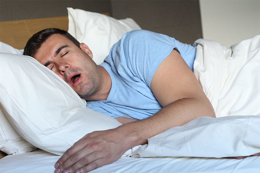 man in blue t-shirt laying on his side snoring in bed
